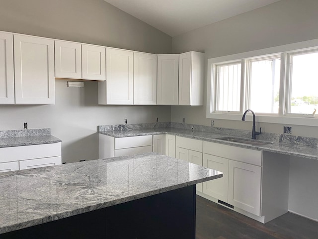 kitchen with light stone counters, white cabinetry, sink, and vaulted ceiling