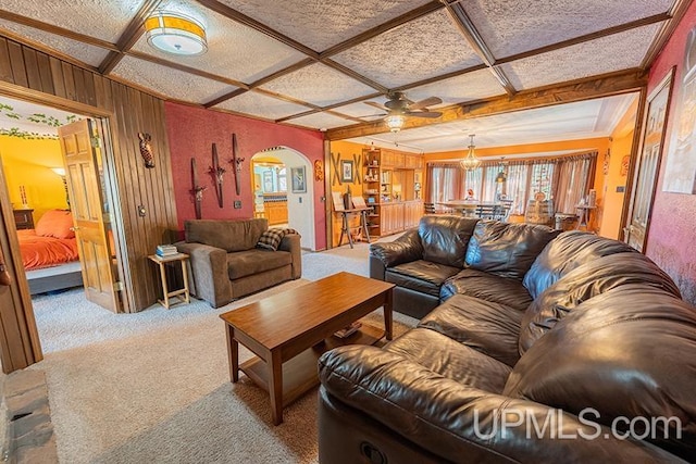 living room featuring carpet floors, coffered ceiling, ceiling fan, and wood walls