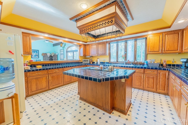 kitchen featuring a center island, black electric stovetop, tile counters, a kitchen bar, and a raised ceiling