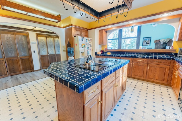 kitchen with black electric stovetop, tile countertops, a center island, and white fridge with ice dispenser