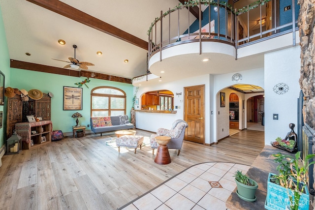 living room with hardwood / wood-style flooring, a towering ceiling, ceiling fan, and beam ceiling