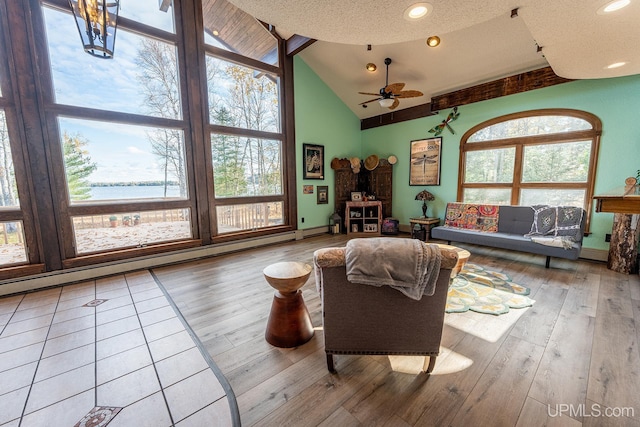 living room with ceiling fan, a water view, wood-type flooring, a textured ceiling, and a baseboard radiator