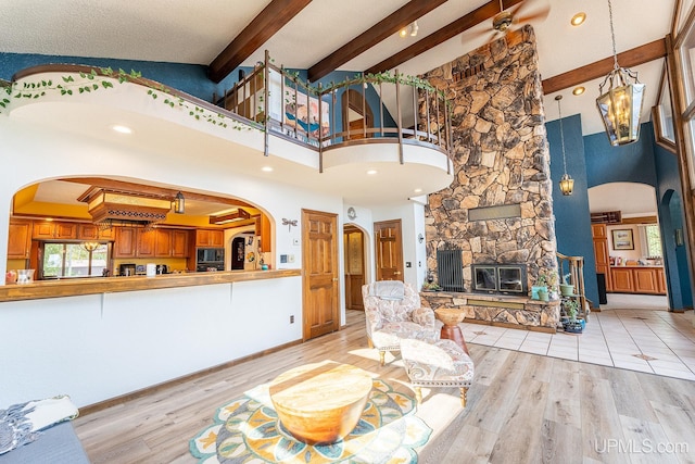 living room featuring beamed ceiling, a stone fireplace, a towering ceiling, and light hardwood / wood-style floors