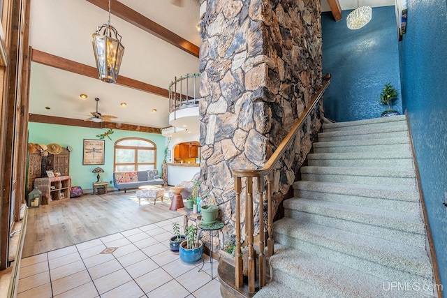 stairway with a high ceiling, ceiling fan, tile patterned floors, and beam ceiling