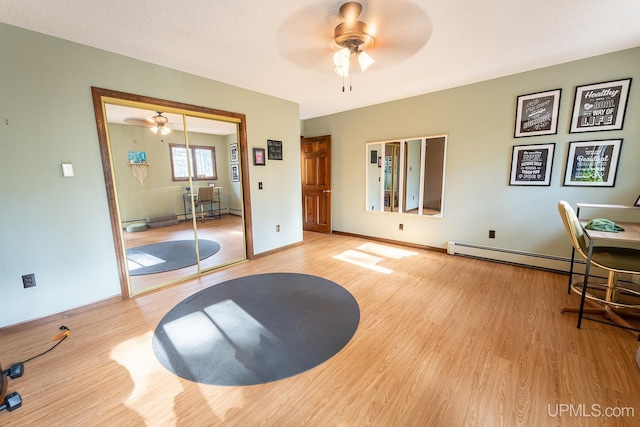 workout room featuring ceiling fan, baseboard heating, and light hardwood / wood-style flooring