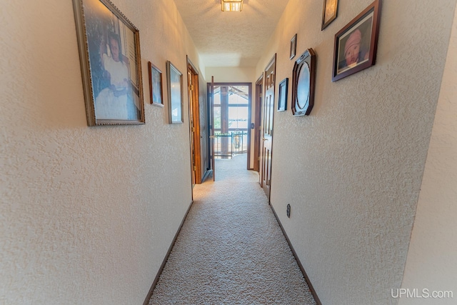 hallway with light colored carpet and a textured ceiling