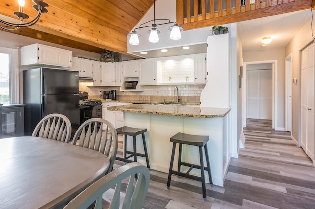 kitchen with black fridge, white cabinets, backsplash, and wood-type flooring