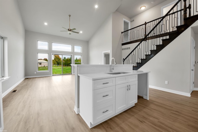 kitchen with a center island with sink, light hardwood / wood-style flooring, high vaulted ceiling, sink, and ceiling fan