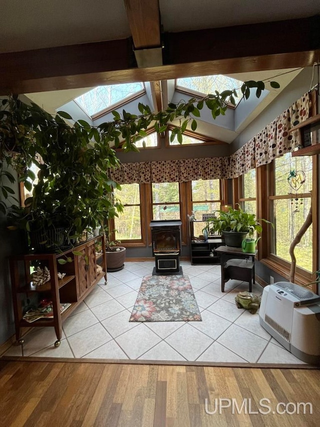 sunroom / solarium with a healthy amount of sunlight, vaulted ceiling with skylight, and a wood stove