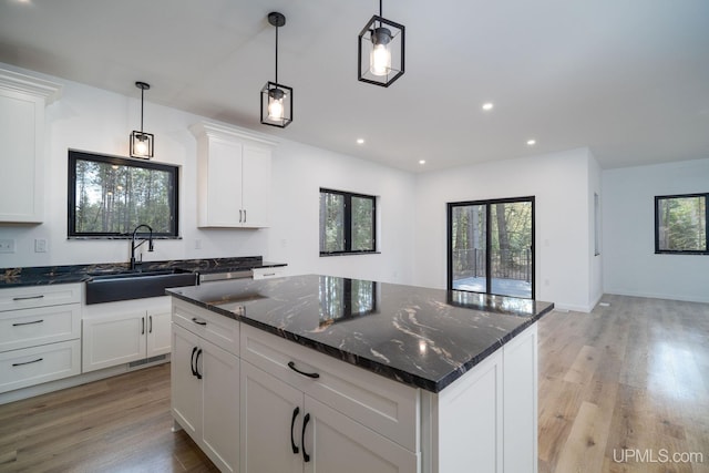 kitchen with a center island, dark stone countertops, sink, light hardwood / wood-style floors, and white cabinetry