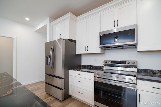 kitchen featuring appliances with stainless steel finishes, light wood-type flooring, dark stone counters, and white cabinets