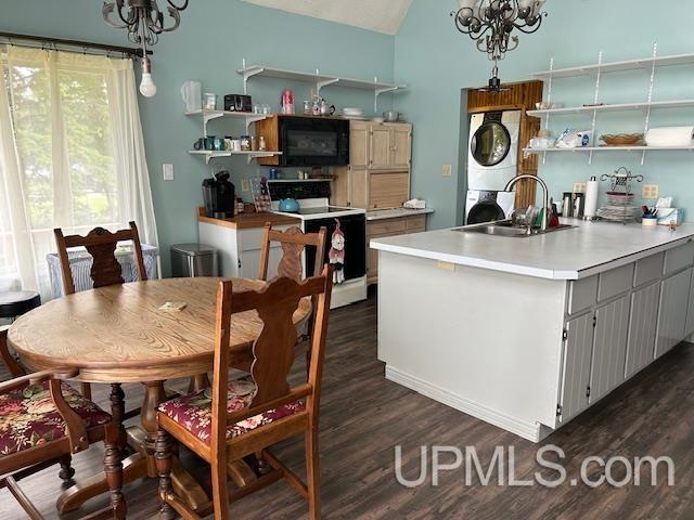 kitchen with dark wood-type flooring, stacked washer and dryer, sink, a notable chandelier, and electric stove