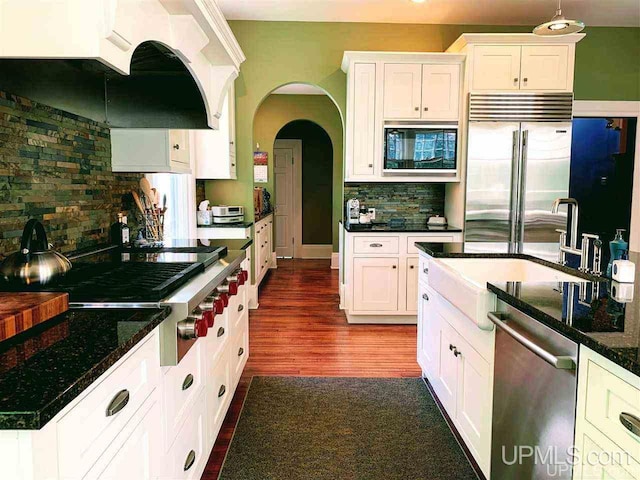 kitchen featuring white cabinetry, dark stone counters, dark hardwood / wood-style floors, built in appliances, and tasteful backsplash