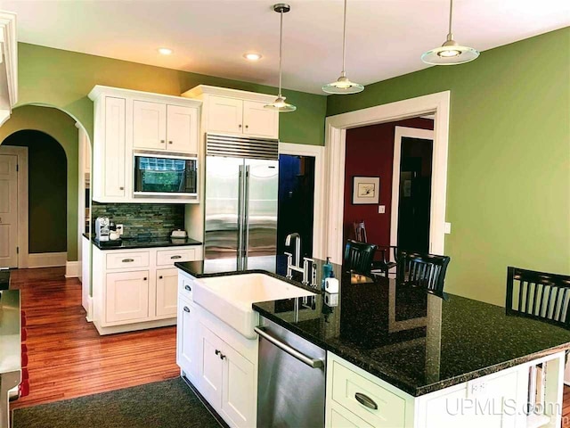 kitchen featuring a kitchen island, white cabinets, hardwood / wood-style flooring, built in appliances, and backsplash