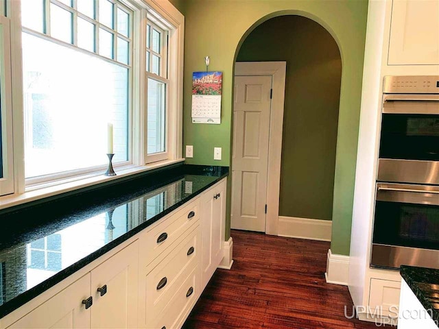 kitchen featuring double oven, dark stone countertops, white cabinets, and dark hardwood / wood-style flooring