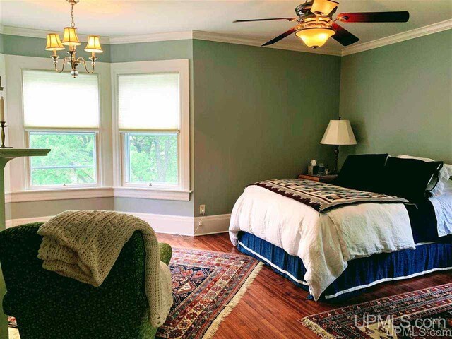 bedroom featuring dark wood-type flooring, ornamental molding, and ceiling fan with notable chandelier