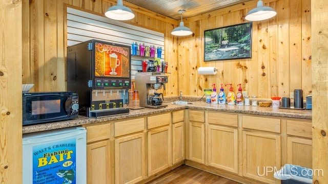 kitchen featuring decorative light fixtures, light brown cabinetry, light hardwood / wood-style floors, fridge, and wooden walls