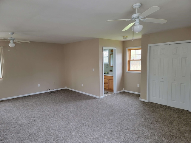 unfurnished bedroom featuring ceiling fan, a closet, dark carpet, and ensuite bathroom