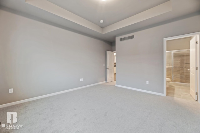 unfurnished bedroom with a raised ceiling, connected bathroom, and light colored carpet