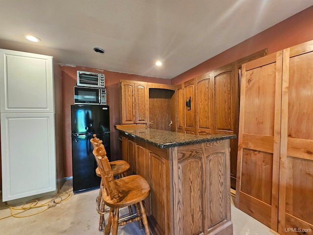 kitchen featuring dark stone counters, black fridge, a center island, and a breakfast bar area