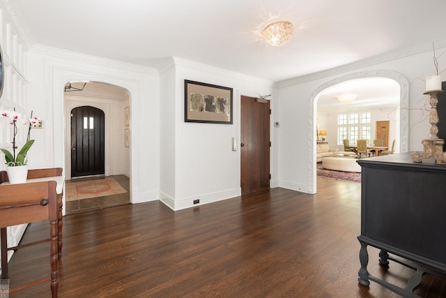 foyer entrance featuring ornamental molding, arched walkways, dark wood finished floors, and baseboards