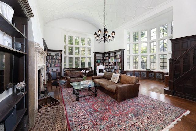 living room with a towering ceiling, an inviting chandelier, a fireplace, and wood finished floors