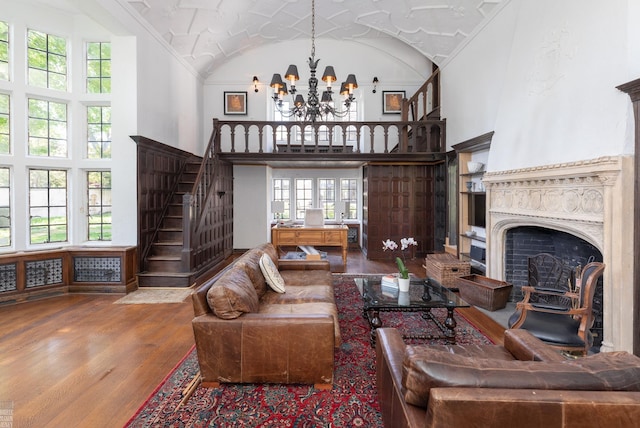 living room featuring a fireplace, an inviting chandelier, wood finished floors, high vaulted ceiling, and stairs