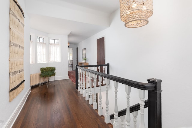 hallway featuring baseboards, radiator heating unit, wood finished floors, an upstairs landing, and a notable chandelier