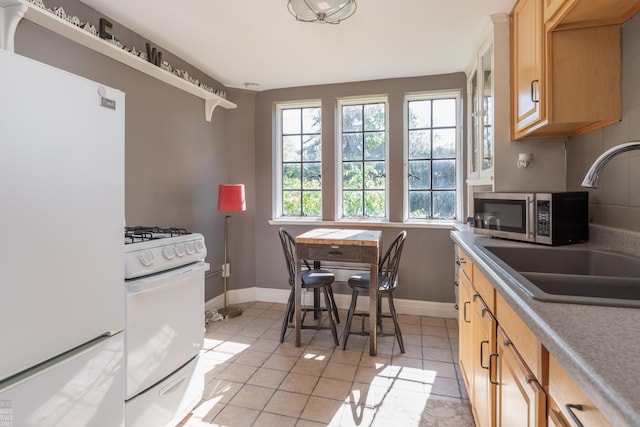 kitchen featuring white appliances, light tile patterned floors, baseboards, and a sink