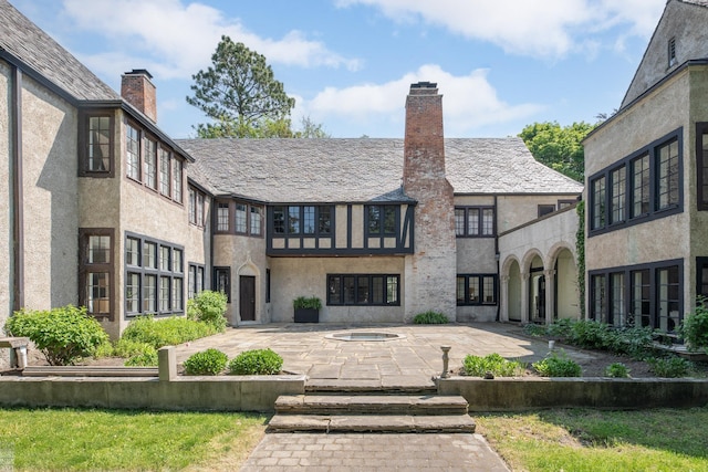 rear view of property featuring a patio area, a chimney, and stucco siding