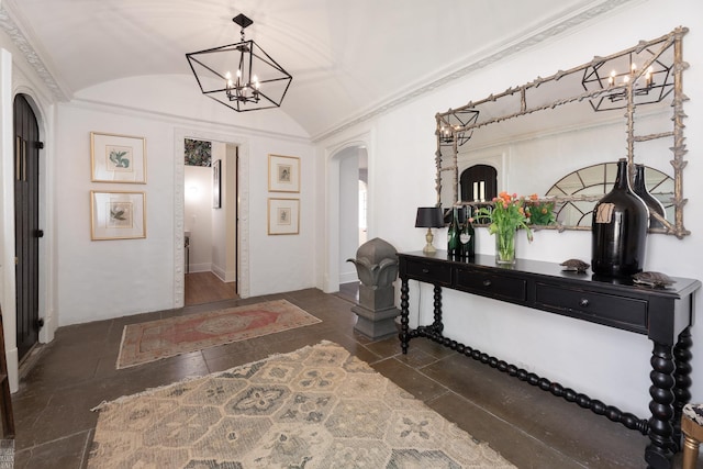 foyer featuring arched walkways, ornamental molding, vaulted ceiling, stone tile flooring, and a notable chandelier