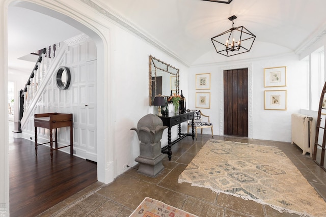 foyer featuring arched walkways, vaulted ceiling, stairs, ornamental molding, and radiator heating unit