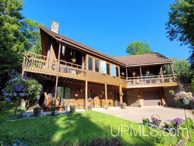 back of property featuring a chimney, concrete driveway, a lawn, an attached garage, and a wooden deck