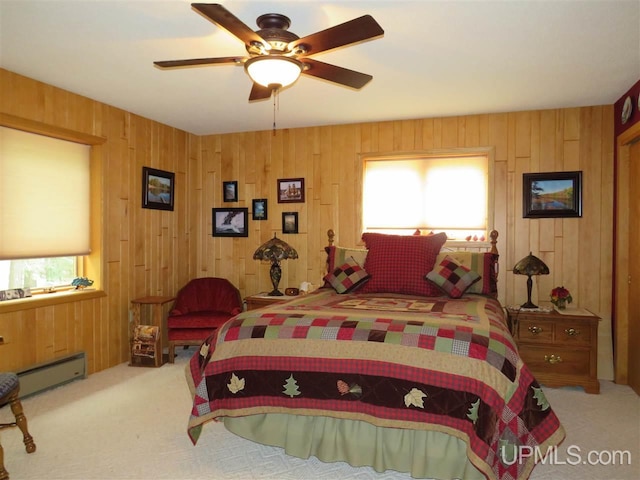 carpeted bedroom featuring ceiling fan, a baseboard radiator, and wooden walls