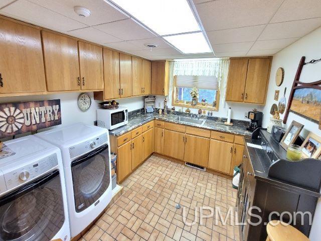 kitchen featuring white microwave, a drop ceiling, a sink, visible vents, and washer and clothes dryer