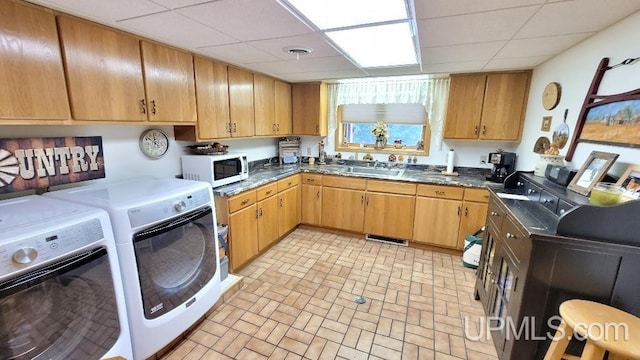 kitchen with dark countertops, white microwave, a sink, a drop ceiling, and independent washer and dryer