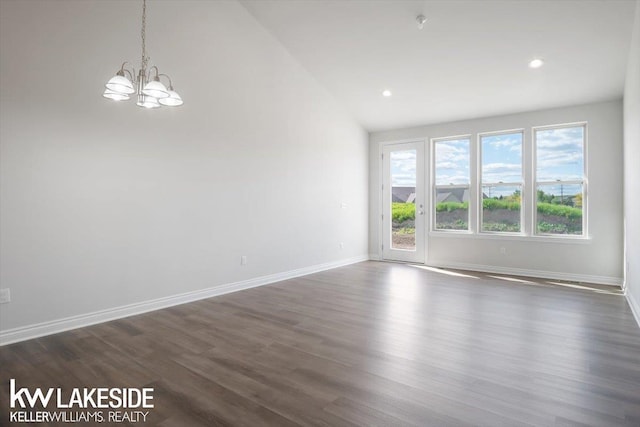 unfurnished room featuring dark hardwood / wood-style flooring, lofted ceiling, and an inviting chandelier