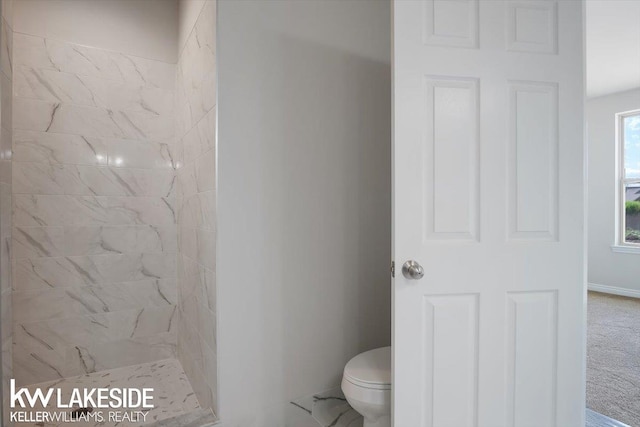 bathroom with a tile shower and toilet