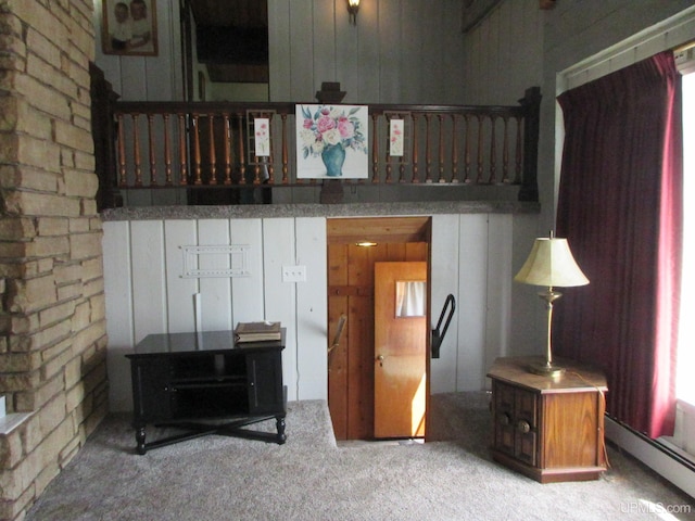 interior space with light colored carpet, a baseboard heating unit, and wood walls