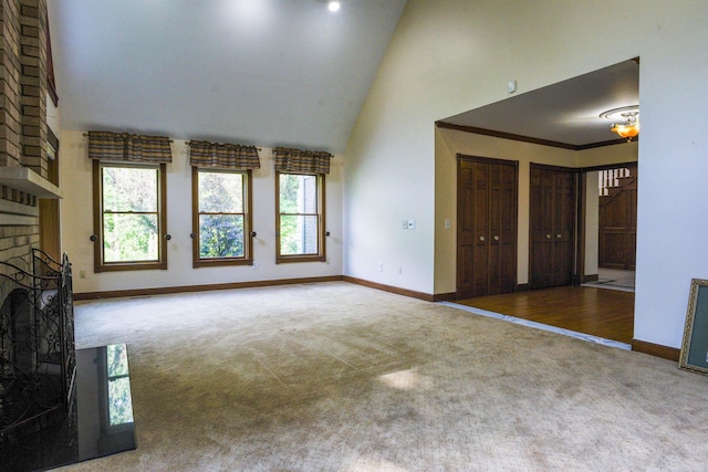 unfurnished living room with high vaulted ceiling, brick wall, a brick fireplace, and dark carpet