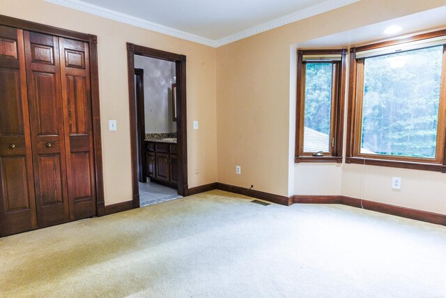 unfurnished bedroom featuring light carpet, ensuite bathroom, and crown molding