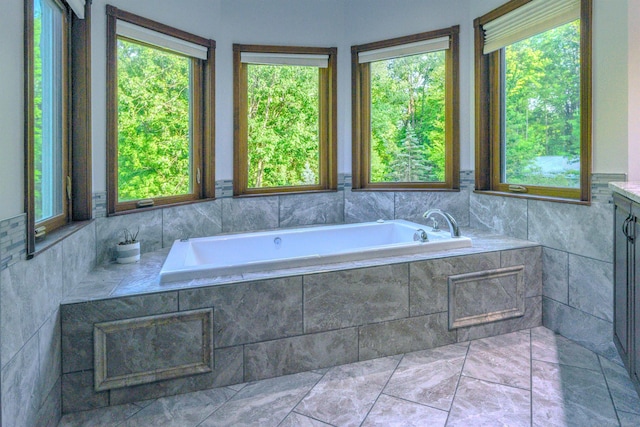 bathroom with tile floors, a wealth of natural light, tiled tub, and vanity