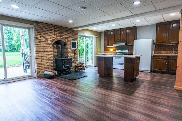 kitchen featuring a paneled ceiling, a wood stove, dark hardwood / wood-style floors, a kitchen island, and white appliances