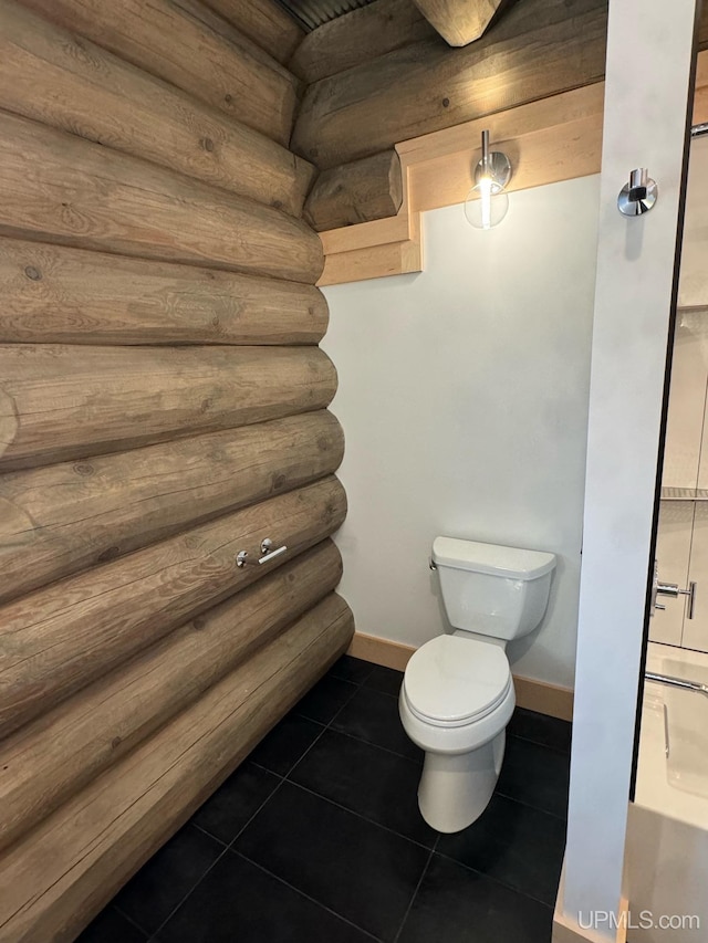 bathroom featuring rustic walls, baseboards, toilet, and tile patterned floors