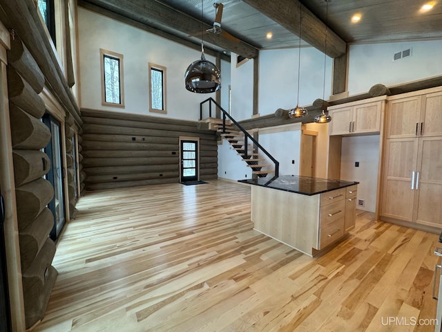 kitchen featuring high vaulted ceiling, light brown cabinetry, dark countertops, and visible vents