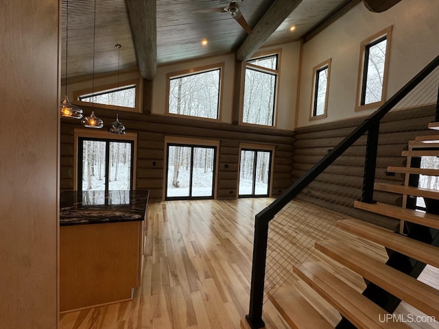 interior space featuring a towering ceiling, stairway, light wood finished floors, beamed ceiling, and rustic walls