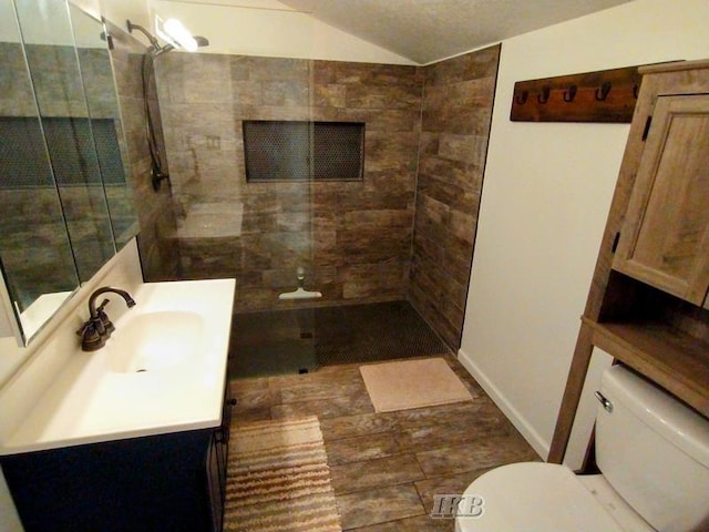 bathroom with vanity, lofted ceiling, toilet, a textured ceiling, and tiled shower