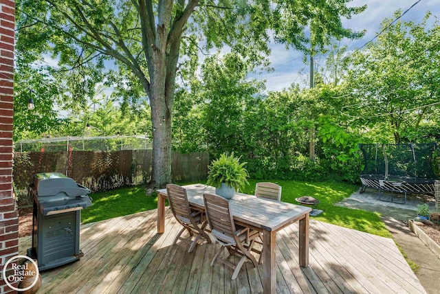 wooden terrace featuring a lawn, a grill, and a trampoline