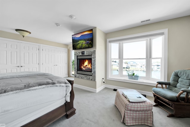 bedroom featuring a fireplace, light carpet, and two closets