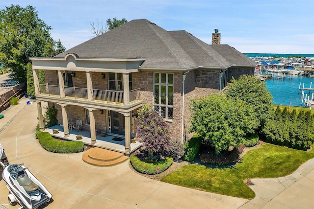 rear view of property with a water view, a chimney, a balcony, a patio area, and stone siding